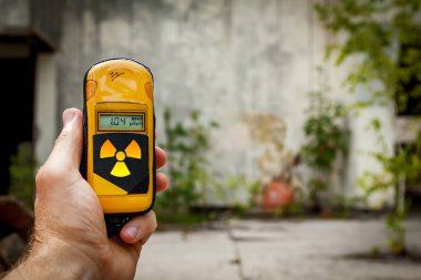 Eski bir taş duvarın arkasında radyasyon seviyesini ölçmek için sarı bir alet tutan bir adam..