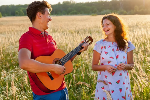Gitarlı genç bir adam güneşli bir günde hamile karısının yanında duruyor. Doğada hamile aile fotoğrafı çekimi.