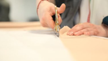 Kadınların elleri beyaz bir masanın üzerinde terzi makası ile kağıdın desenini kesiyor. Kumaş, eller, dikiş, tasarım