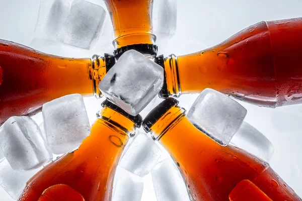 Soda glass bottles in a refrigerated ice cubes on a light background