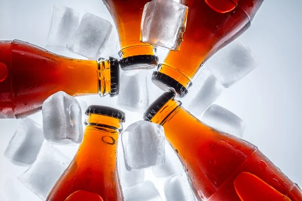 Soda glass bottles in a refrigerated ice cubes on a light background