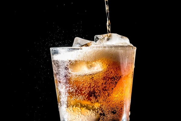 Corriente de soda que se vierte en un vaso con soda y cubo de hielo sobre fondo negro, textura de primer plano, salpicaduras, salpicaduras, fizz —  Fotos de Stock