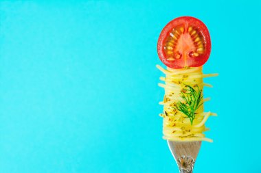 Spagetti makarna fesleğen ve kiraz domates mavi zemin üzerine bir parça ile bir çatal yarası yeşil sapı ile