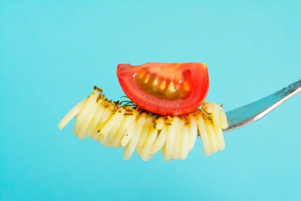 Паста Спагетті з базиліком і гілочкою зелені, намотаною на виделку з шматочком вишневих помідорів на синьому фоні — стокове фото