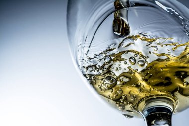 Beyaz şarap bir bardak dökme, gri arka plan üzerinde beyaz şarap sıçrama akışı