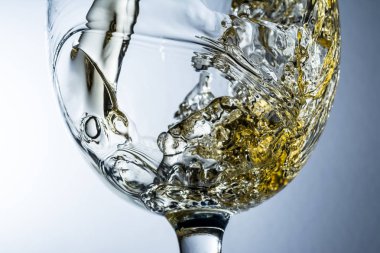 Beyaz şarap bir bardak dökme, gri arka plan üzerinde beyaz şarap sıçrama akışı