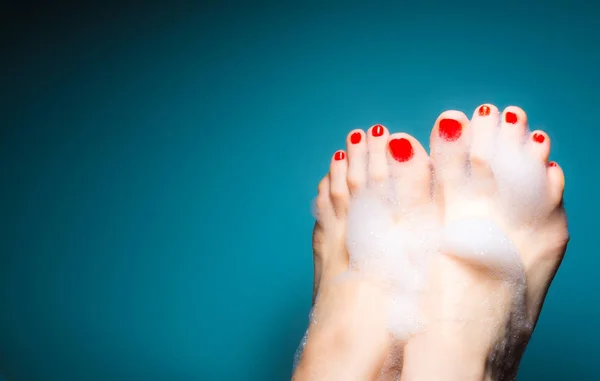 파란색 배경에 두꺼운 거품에 있는 붉은 손톱으로 젊은 여자의 발 — 스톡 사진