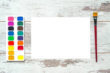 Renkli Boya fırçaları ve bir beyaz izole kağıt yaprağı, guaş, eski bir vintage ahşap arka plan üzerine suluboya, çatlaklar ahşap aşınmış panoları ile. Üstten Görünüm.