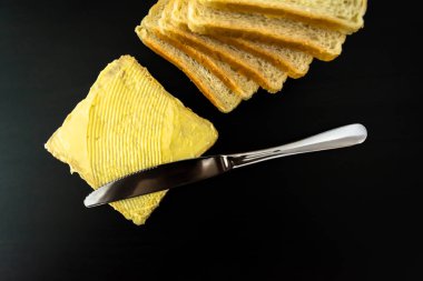 Tereyağı ile güzel lekeleri ve bıçakla ekmek yakın çekim karanlık bir arka plan üzerine bir parça