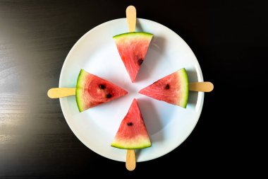 bir sopa dondurma yakın siyah bir zemin üzerine beyaz plaka üzerinde çekim üzerinden dilim karpuz kesmek