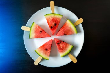 bir sopa dondurma yakın bir koyu mavi zemin üzerine beyaz plaka üzerinde çekim üzerinden dilim karpuz kesmek