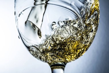 Beyaz şarap sıçrama yakın çekim makro gri arka plan, beyaz şarap bir bardak dökme akışı üzerinde.