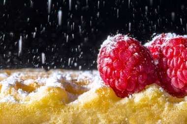 Ahududu ve eleme dökme toz şekeri üretme, siyah bir zemin üzerine güneş ışığı yakın çekim makro ile tatlı tost waffle