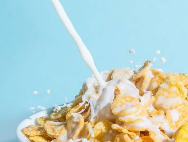 Ornflakes yakın çekim ile bir kase içine dökülen süt akışı. Süt sıçrama ile pul makro mavi bir arka plan üzerinde bir Kupası.