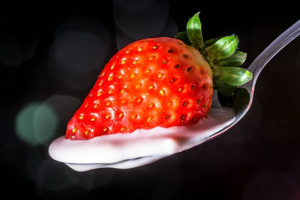 Fragola su un cucchiaio con crema di yogurt rosa fragola primo piano con riflessi di luce solare su uno sfondo nero — Foto Stock