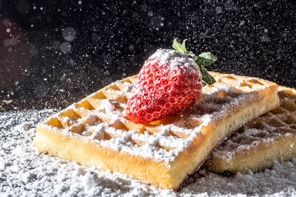 Doces waffles torradas com morango com folhas em cima e peneirando verter açúcar em pó na luz solar macro close-up em um fundo preto — Fotografia de Stock