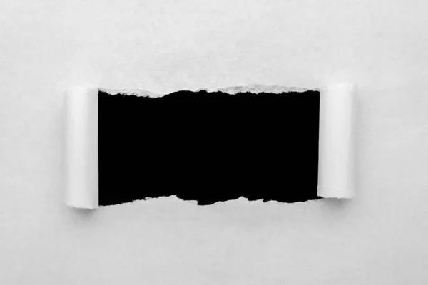 A hole in white paper with torn edges and a black isolated background inside.