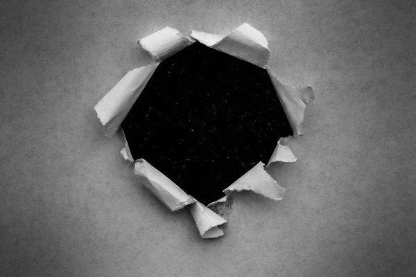 Un agujero en papel vintage con bordes rotos de cerca con un fondo negro en el interior con coloridas estrellas espaciales en el universo . — Foto de Stock