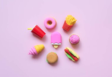 Çeşitli oyuncaklar fast food ve minyatür şekerlemeler. Yumuşak pembe arka planda gölgeler..