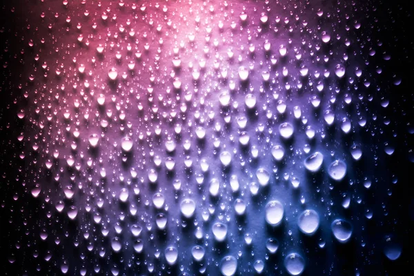 Druppels water met een mooi glad verloop in roze en blauwe kleuren close-up macro op het materiaal in het zonlicht. — Stockfoto