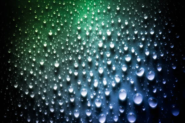Druppels water met een mooi glad verloop in groene en blauwe kleuren close-up macro op het materiaal in het zonlicht. — Stockfoto
