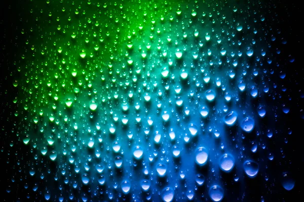 Druppels water met een mooi helder verloop in groene en blauwe kleuren close-up macro op het materiaal in het zonlicht. — Stockfoto