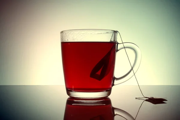 Sachet de thé dans une tasse transparente avec réflexion sur un fond gris. Vieille photo vintage de style rétro grunge . — Photo