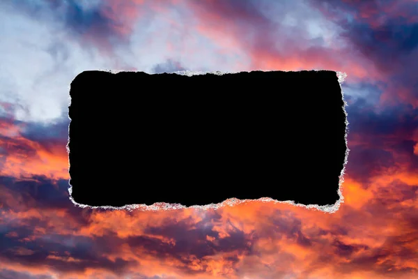 A hole in the sunset sky with torn edges, as on paper, with an isolated black copyspace background in the center. Concept of global climate change on Earth, global warming, a hole in space and time.