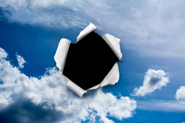 A hole in the day sky with torn edges, as on paper, with an isolated black copyspace background in the center. The concept of global climate change on Earth, global warming, a hole in space and time.