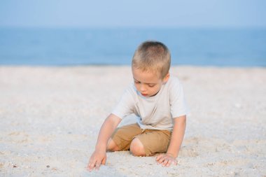 Kum deniz kenarında oynarken küçük çocuk gülümseyen portre okyanus. Olumlu insan duyguları, duygular, joy. Tatil yapma ve yaz zevk komik şirin çocuk.