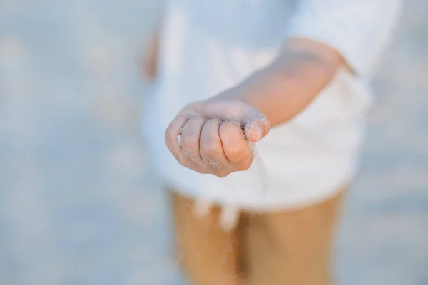 The child holds sand in the hands of the beach near the sea