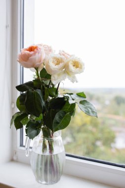 Pencere kenarındaki cam vazoda gül buketi 