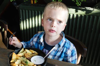 Boş bir levha ile önünde oturan bir restoranda sıkılmış küçük çocuk. Yemekte patates yemek sırasında rahatsız küçük çocuk