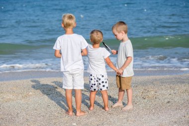 Arkadan Görünüm plajda üç kardeşin. Deniz kenarında tatil zevk mutlu bir aile. Kumlu Sahilde yürüyüş üç kardeş. Üç erkek arkadan görünüm. açık havada.