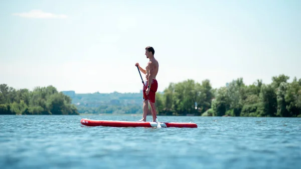 SUP silhueta de homem atlético paddle embarque ao pôr do sol — Fotografia de Stock