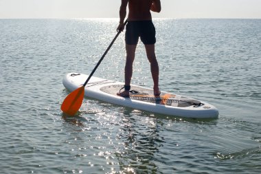 Sup siluet spor adamı gün batımında sörf yapıyor.