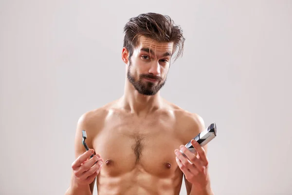 若い男は 古典的な電気カミソリを保持しています 彼は彼のひげを剃ることを使用する つを決定することです — ストック写真
