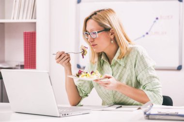 İşkadını ofisinde salata yiyor. 
