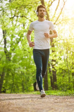 Genç adam parkta koşu. Kulaklıklar müzik dinleme o. 