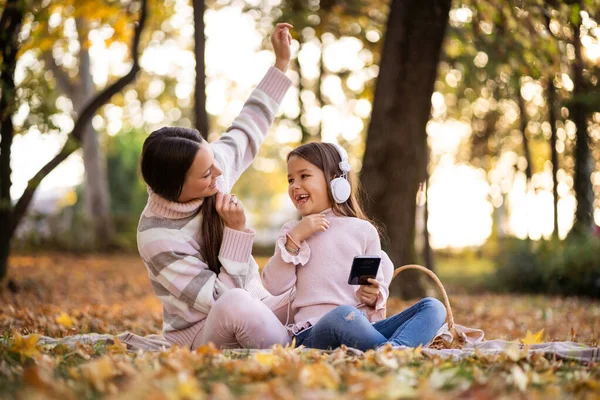 妈妈和女儿在公园里享受秋天 他们在耳机上听音乐 — 图库照片