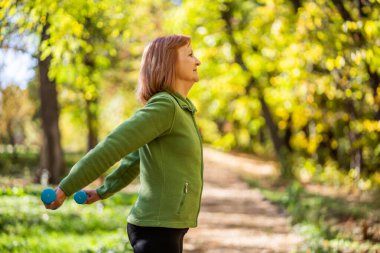 Kıdemli kadın güneşli bir günde parkta ağırlık egzersizi yapıyor..