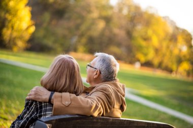 Romantik son sınıf çifti parkta bankta oturuyor ve sonbaharın tadını çıkarıyor..