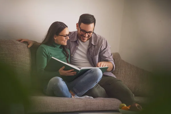 Pareja Feliz Está Sentada Sofá Casa Mirando Libro — Foto de Stock