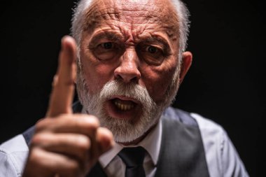 Portrait of angry senior man who threatens. Black background. clipart