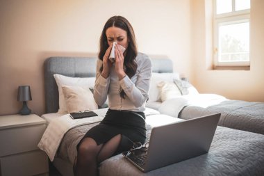 İş seyahatinde çok çalışan bir iş kadını otel odasında oturuyor ve dizüstü bilgisayarla çalışıyor. Alerjisi var..