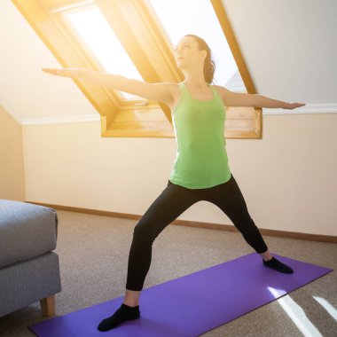 Genç kadın evde yoga yapıyor. Savaşçı pozu / Virabhadrasana