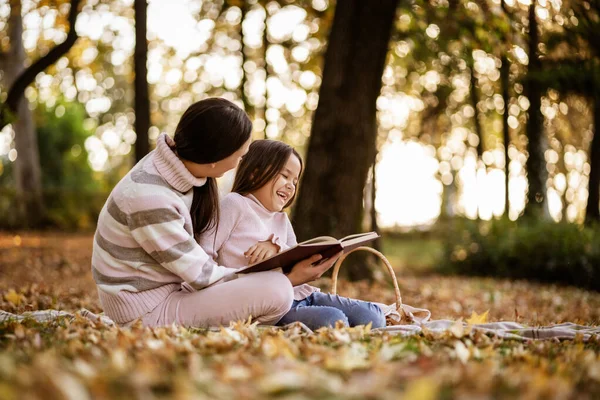 Mother and daughter enjoying autumn in park. Little girl is learning to read.