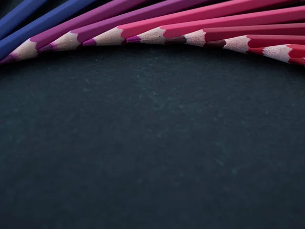 Set of colored pencils arranged in a wheel on slate background. close up