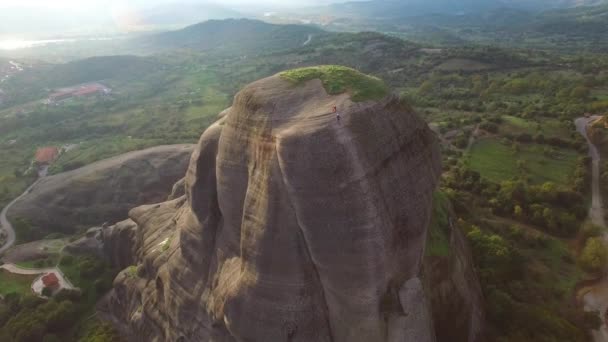 ギリシャ メテオラの切り立った岩肌の崖の顔を登る登山家として美しい航空 — ストック動画