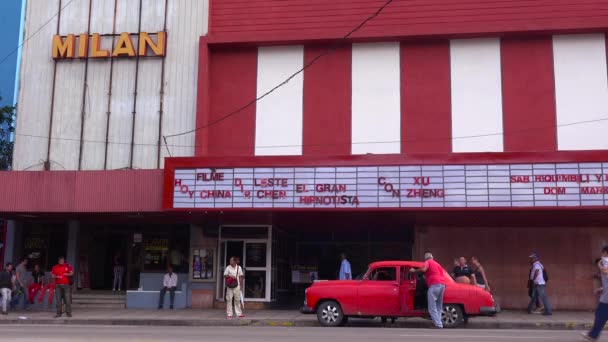 男性はキューバのハバナにある映画館の外で古い車をロードします — ストック動画